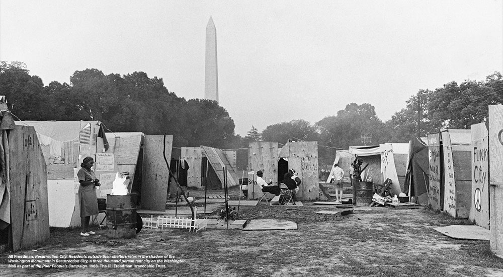 Jill Freedman, Resurrection City. Residents outside their shelters relax in the shadow of the Washington Monument in Resurrection City, a three thousand person tent city on the Washington Mall as part of the Poor People’s Campaign. 1968. The Jill Freedman Irrevocable Trust.